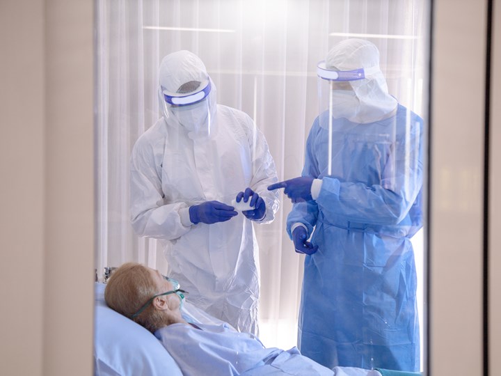 Ärzte mit Schutzkleidung bei im Bett liegender Patientin