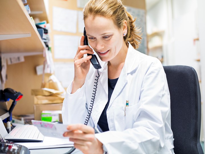 Ärztin telefoniert und blickt auf Zettel in der Hand