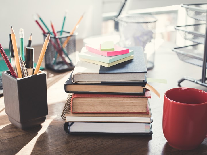 Vollgeräumter Schreibtisch mit Büchern, Stiften, Kaffeetasse