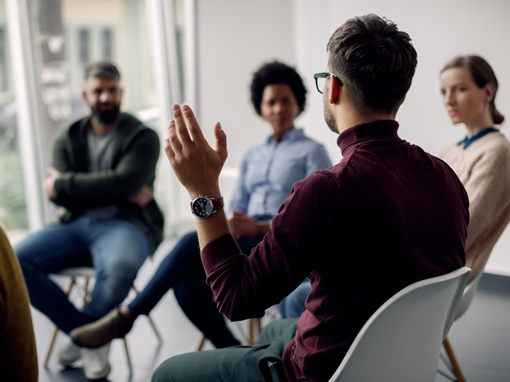 Mann hebt in Gruppentherapie die Hand (Rückansicht)